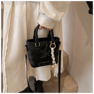 Detail of black mini handbag with gold metal handle and decorative striped silk scarf charm