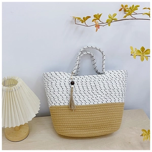 Detail of woven straw tote bag featuring bicolor design and tassel with wooden beads