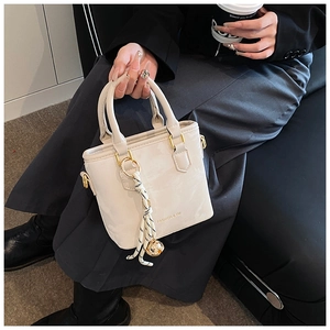 Detail of a chic cream mini tote bag with striped charm held by a model in a casual setting