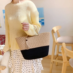 Close-up of two-tone woven straw tote bag featuring a decorative tassel charm