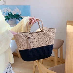 Detail of two-tone woven tote bag featuring beige and navy stitching with tassel accent
