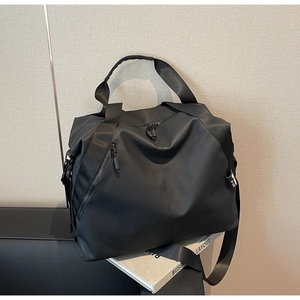 Detail view of black travel bag with dual handles and adjustable shoulder strap on sofa