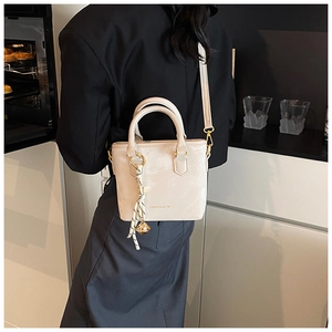 Detail of a creamy glossy handbag featuring fashion lettering and a striped scarf charm