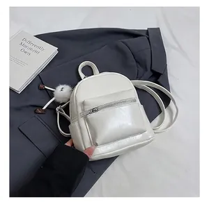 Detailed view of white mini leather backpack with a cute fuzzy eye charm on a blazer