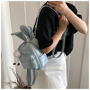 Detail of light blue backpack with rabbit ears and plush pompom on a faux leather texture