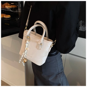 Detail of cream white tote bag with woven charm and golden hardware in lifestyle setting