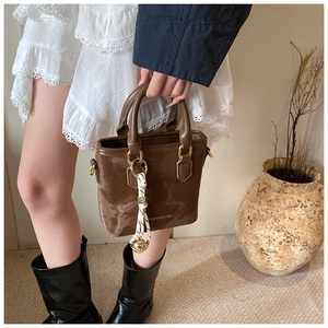 Close-up of premium brown leather handbag featuring a stylish woven rope tassel charm