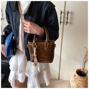 Close-up of brown retro mini bucket bag with glossy PU finish and woven charm detail