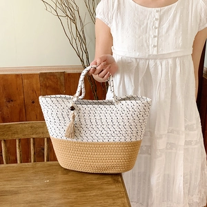 Detail of woven straw tote bag featuring wood bead tassel and dual round handles