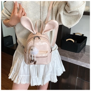 Detail of light pink mini backpack with bunny ears and plush charm on a model