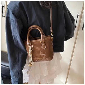Detail of a brown marble textured bucket bag featuring gold hardware and a creative tassel