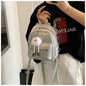 Detail of light gray patent leather mini backpack with a white plush eye-shaped charm