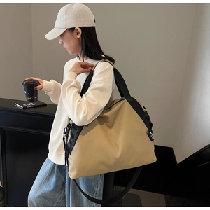 Detail of the large beige tote bag with black strap and side zipper in a casual setting
