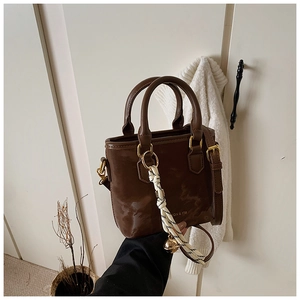 Detailed view of deep brown faux leather handbag with golden hardware and bell charm