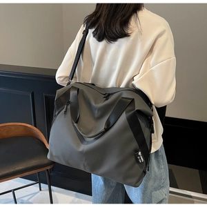 Rear view of a spacious grey travel tote bag with black straps on a female model