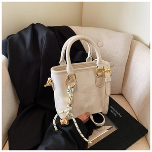 Detail of white leather handbag with golden hardware and braided charm on a beige sofa