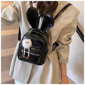 Close-up of black mini bunny ear backpack with plush charm worn by model on stairs