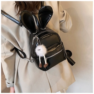Detail view of mini black patent leather backpack with bunny ears and plush monster charm