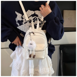 Close-up of a white mini PU leather backpack with a cute monster plush charm detail