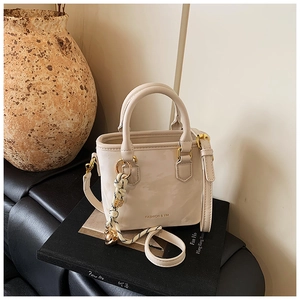 Close-up of cream mini tote bag with gold lettering and woven charm on black books