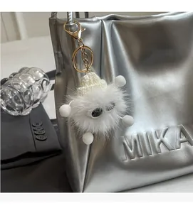 Detail of white furry monster charm with knit hat on a silver tote bag as accessory
