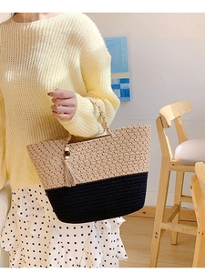 Handcrafted woven straw tote bag with black accents and decorative wooden bead tassel