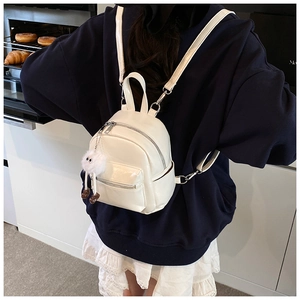 Detailed close-up of a mini white patent leather backpack with a cute plush charm