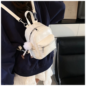Macro detail of white glossy mini backpack with silver metal zipper and plush ball charm