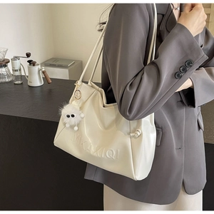 Detail of cream white faux leather tote with embossed logo and plush monster keychain