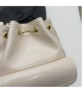 Dettaglio della borsa a secchiello beige con occhielli e coulisse in catena dorata