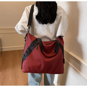 Detail of red travel tote bag with black handles and side zipper pocket closeup