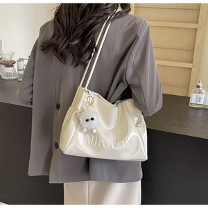 Detailed view of white glossy PU shoulder bag with embossed logo and plush charm