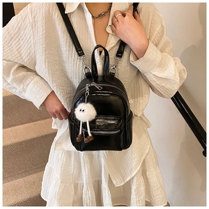 Glossy black mini backpack with plush pendant detail shown in an outdoor lifestyle setting