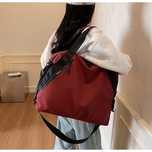 Detail view of burgundy waterproof nylon travel bag with black wide straps on model