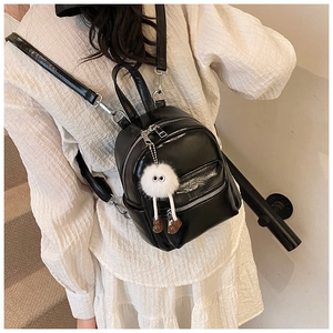 Detail of black glossy leather mini backpack with cute plush doll charm on shoulder