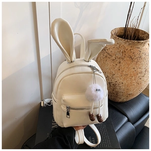 Close-up of white mini backpack with rabbit ears and plush monster charm against a pot
