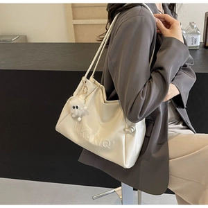 Close-up of beige glossy leather tote bag with embossed letters and plush charm detail