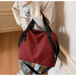 Side view of dark red large capacity travel bag with black shoulder strap worn by model