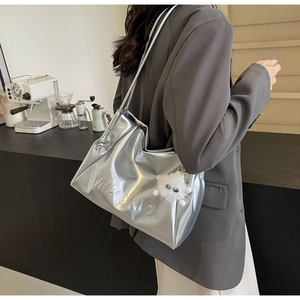 Detailed close-up of metallic silver shoulder bag with MIKAKIQI logo and plush charm