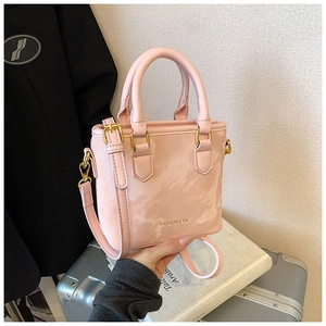Pink patent leather handbag with gold buckles and adjustable strap shown with luggage