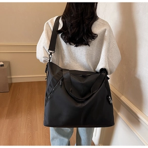 Detail of a large black nylon travel tote showing the adjustable strap and handles on a model