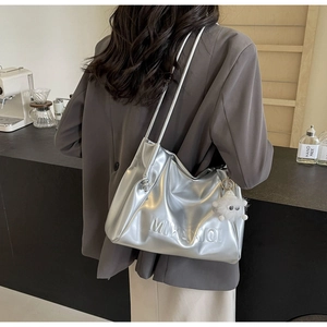 Close-up of metallic silver tote bag with side embossed letters and plush monster charm
