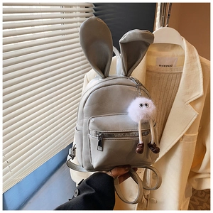 Detail of grey mini backpack with rabbit ears and plush charm in a lifestyle setting