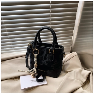 Detail of black textured bucket bag with gold hardware and woven bell charm