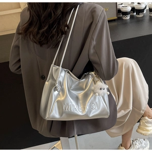 Close-up of silver metallic tote bag featuring embossed logo and a plush charm