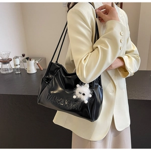 Close-up of black patent leather shoulder bag with embossed logo and fuzzy monster charm