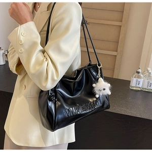 Detail of black leather shoulder bag with embossed letters and white plush monster charm