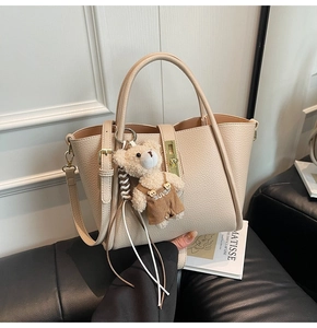 Dettaglio borsa in pelle beige con chiusura a rotazione dorata e ciondolo a orsetto