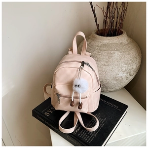Pink faux leather mini backpack with plush charm detail on black books and beige background