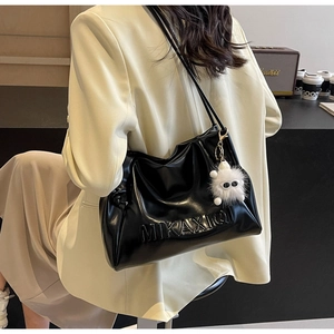 Close-up of glossy black leather tote bag featuring letter embossing and a furry charm